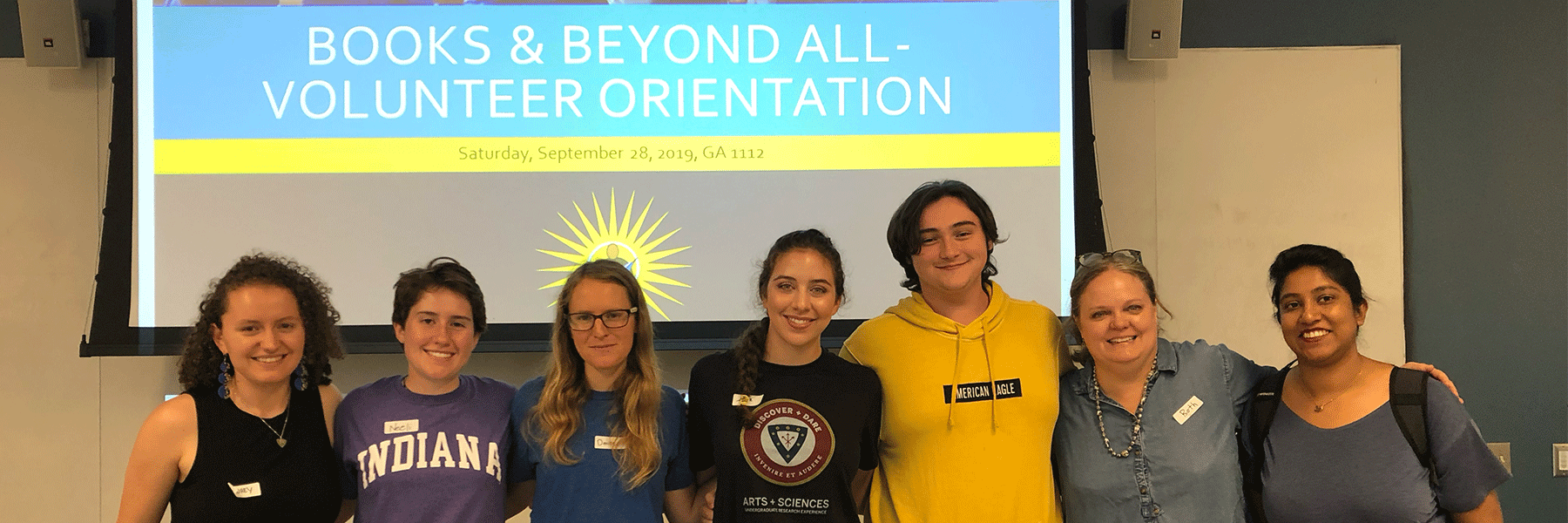 A group of college students pose in front of a screen for volunteer orientation