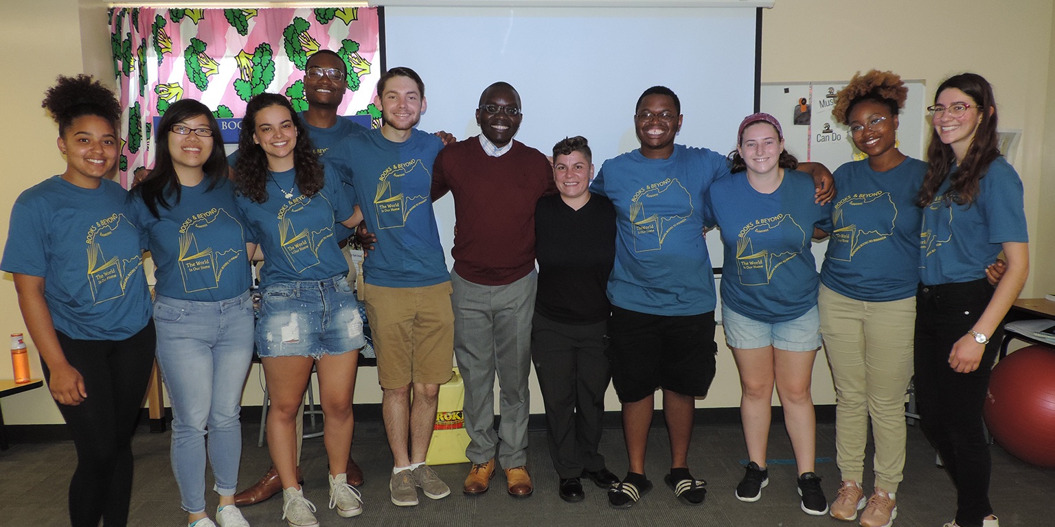 A group of volunteers pose at the front of a classroom with arms around each other's shoulders