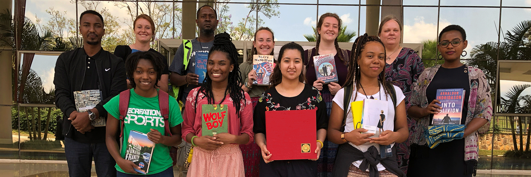 A group of eleven people pose outside a building each holding a book on their arms